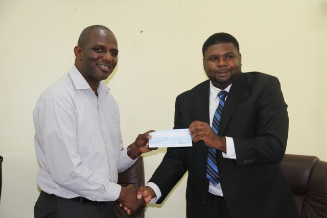 Chief Executive Officer of the St. Kitts and Nevis Sugar Industry Diversification Foundation Mr. Terrence Crossman (left) presenting the first payment from a grant for the Nevis Water Supply Enhancement Project jointly funded by the Caribbean Development Bank and the Administration, to Junior Minister in the Nevis Island Administration Troy Liburd on June 24, 2014 at the Ministry of Finance conference room